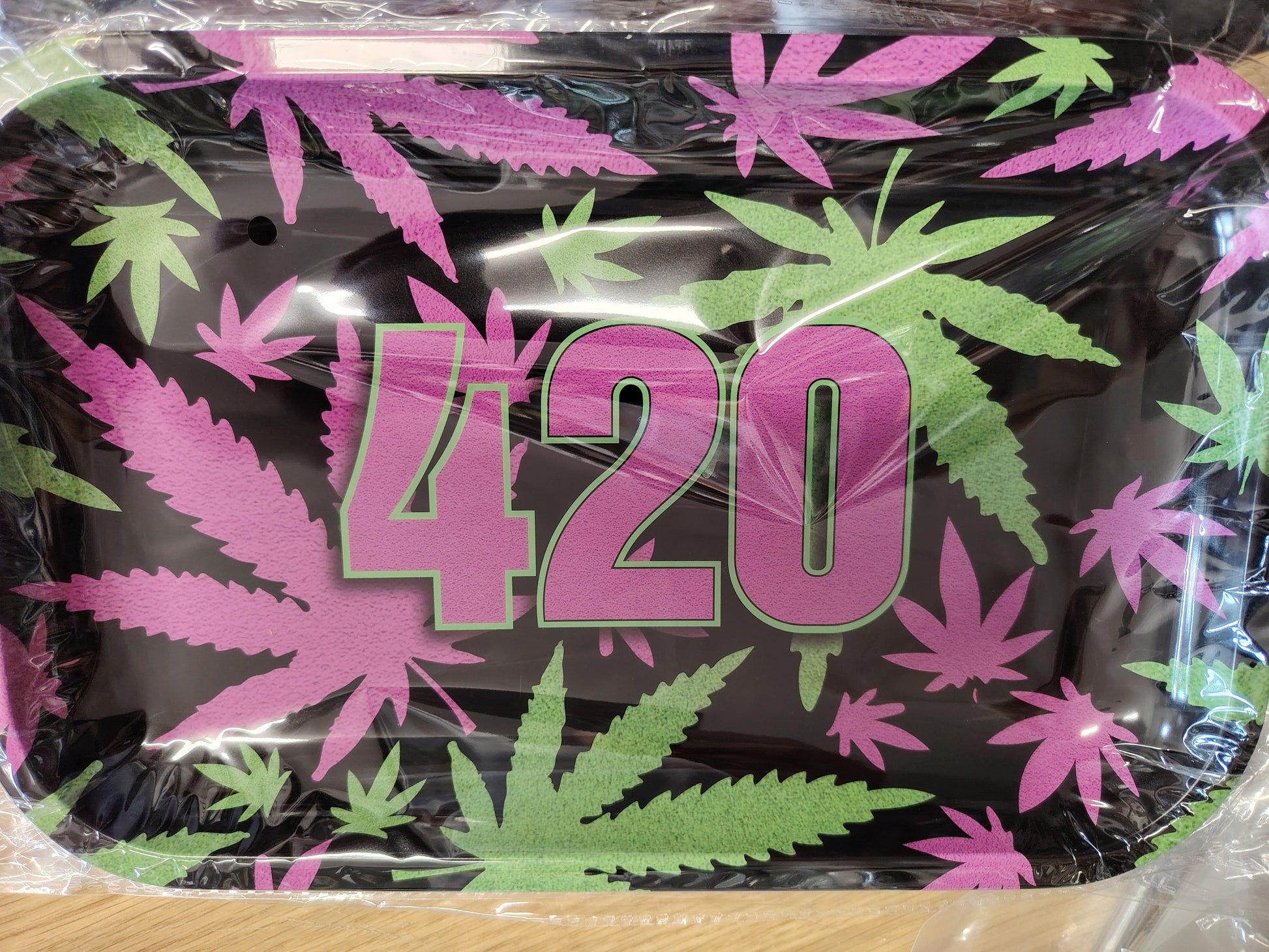 Black tray with pink and green leaf design and '420' text, wrapped in plastic.